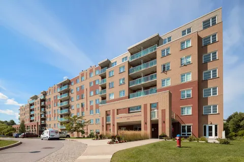 Brick residence building with balconies and a covered entrance beside a driveway