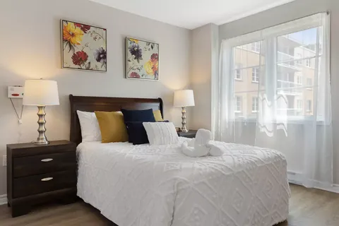 Bedroom with a dark headboard, white bedding, floral artwork and a window