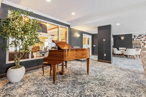 Grand piano beside seating, plants and large interior windows