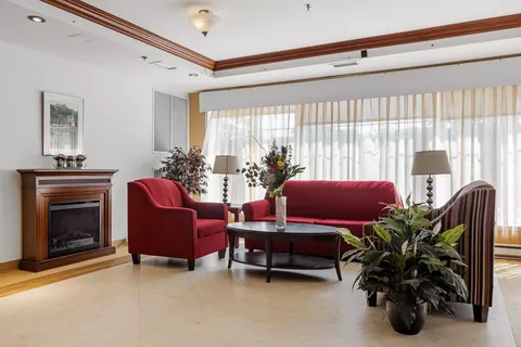Red sofa and armchairs beside a fireplace and broad curtained windows