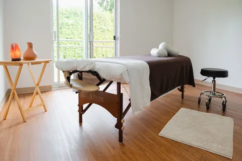Massage room with a treatment table, stool and window.