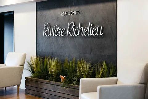 Lobby seating beside a planter and the residence name on the wall.