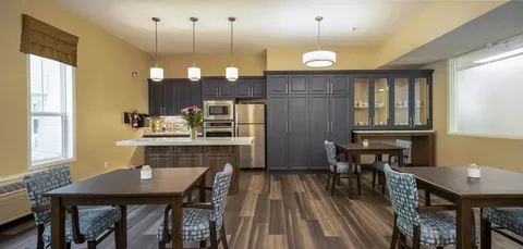 Tables and patterned chairs beside a kitchen with dark cupboards