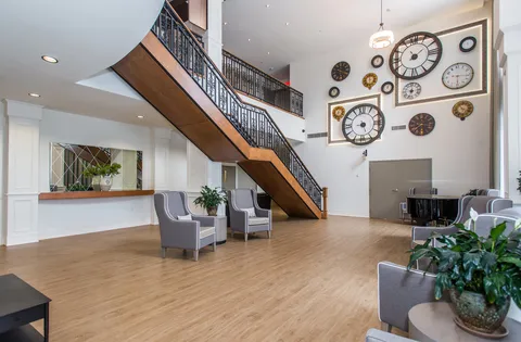 Lobby with armchairs, a piano, a staircase and decorative wall clocks.