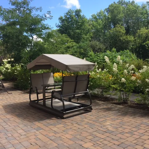 Covered garden swing beside flowering shrubs.