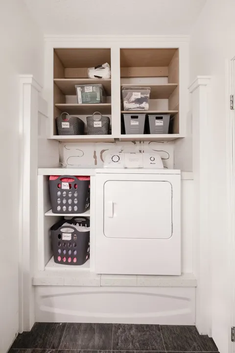 Laundry alcove with a white dryer, baskets and open shelves