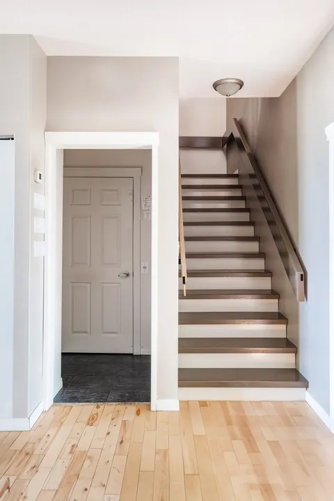 Wooden staircase with railings beside a doorway and pale walls