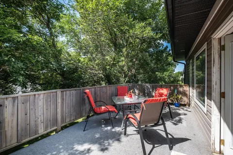 Patio with red chairs, a glass table, wooden fencing and trees