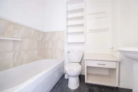 Bathroom with a white bathtub, toilet, vanity and wall shelves