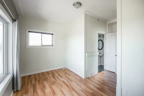 Empty room with wood flooring, two windows and an open bathroom door