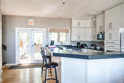 Kitchen with white cabinets, a dark counter, bar stools and glass doors