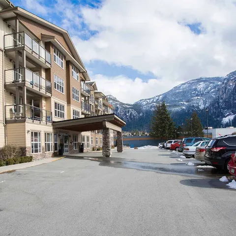 Building with balconies and a covered entrance beside a parking area