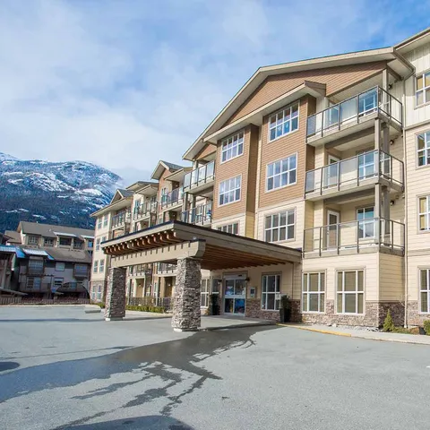 Multi-storey residence with balconies, a covered entrance and mountains behind it