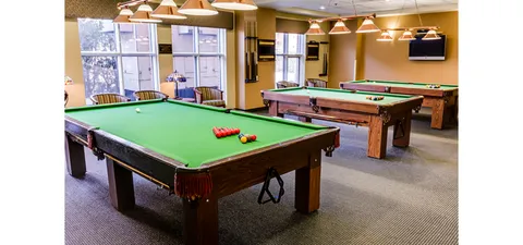 Billiards room with three green pool tables and a dark television screen