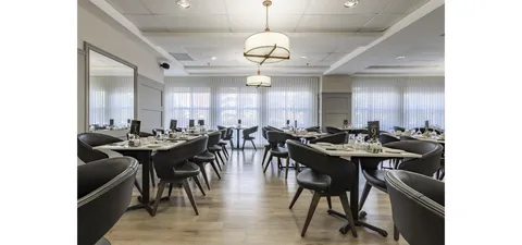Dining room with dark chairs, set tables and sheer window curtains