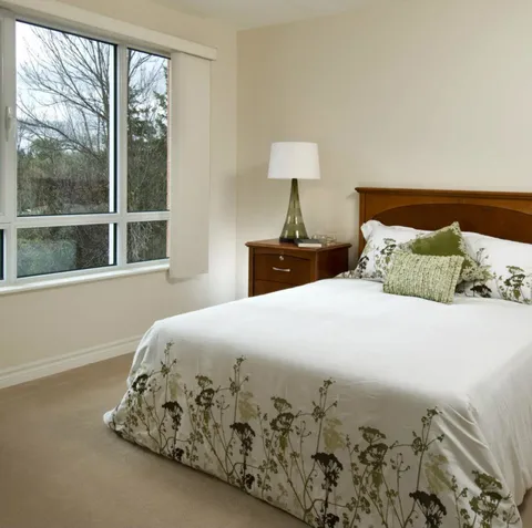 Bedroom with a bed and bedside lamp beside a large window