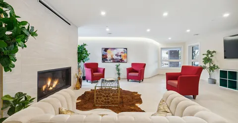 Room with red armchairs, white sofas, a fireplace and an abstract painting