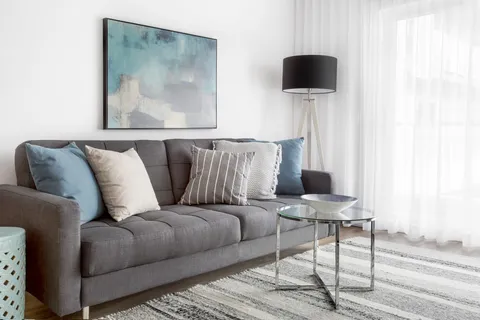 Apartment sitting area with a sofa, cushions, side table and abstract artwork.