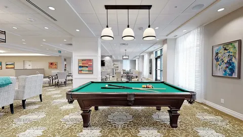 Billiards table beneath pendant lights beside windows
