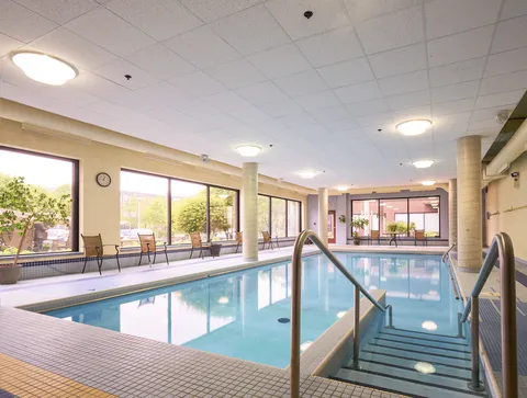 Indoor pool with handrails, large windows and chairs along the far side