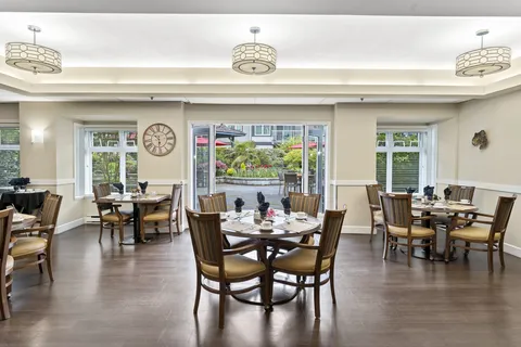 Dining room with round tables, wooden chairs and large windows.