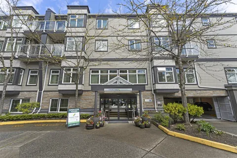 Residence facade with balconies, trees and a paved entrance drive.