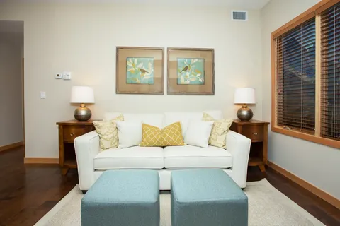 Living room with a sofa, two ottomans, floral wall art and a window.