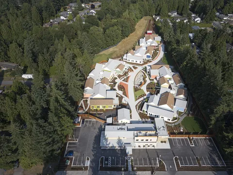 Aerial view of residence buildings, paths, gardens and parking spaces surrounded by trees