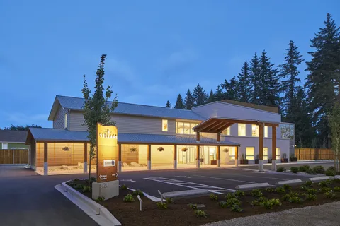 Residence building at dusk with a covered entrance, illuminated windows and an empty parking area