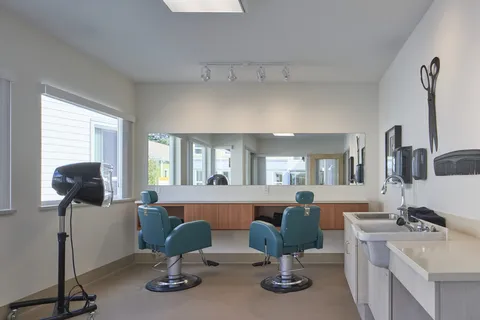 Salon with two turquoise styling chairs, a hooded dryer, sinks and a wide mirror