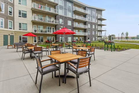 Patio with tables, chairs, red umbrellas and raised garden beds beside the building