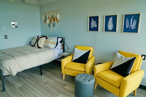Bedroom with a bed, two yellow chairs and framed fern prints
