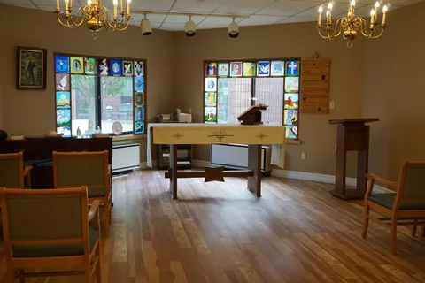 Chapel with rows of chairs, an altar and stained glass windows.
