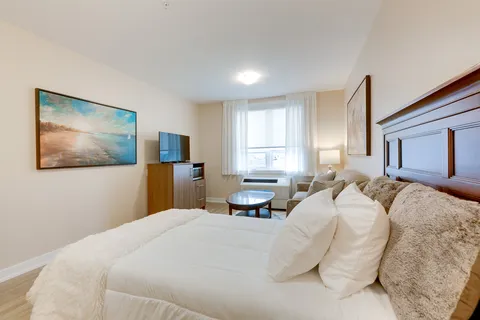 Bedroom with white bedding, a sofa, a glass coffee table and a television