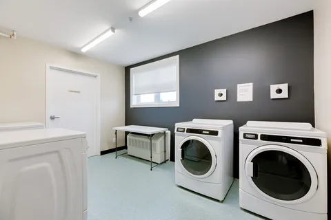 Laundry room with white washers, front-loading dryers and a folding table