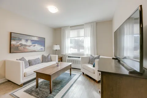 Sitting area with a white sofa, an armchair, a wooden coffee table and a television