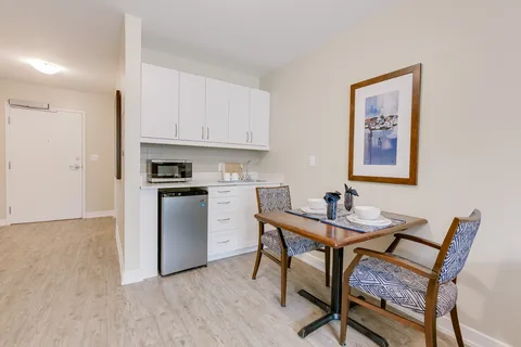 Kitchenette with white cabinets, a microwave, a small fridge and a table for two