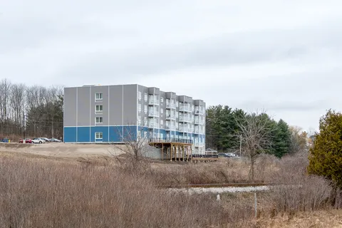 Rear of the residence with white balconies overlooking brush and a small pond
