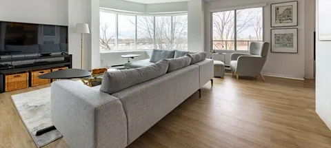 Sitting area with a grey sofa, television, armchair and large windows