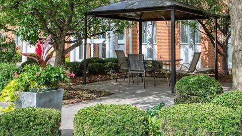 Garden seating under a gazebo beside flowering beds.