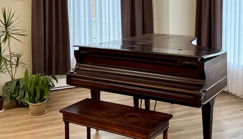 Piano and bench beside a large window.