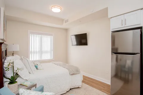 Bedroom with white bedding, a kitchenette and a wall-mounted television