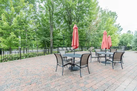 Brick patio with tables, chairs and folded red umbrellas.