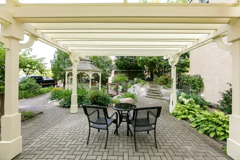 Patio table and chairs beneath a pergola overlooking garden paths