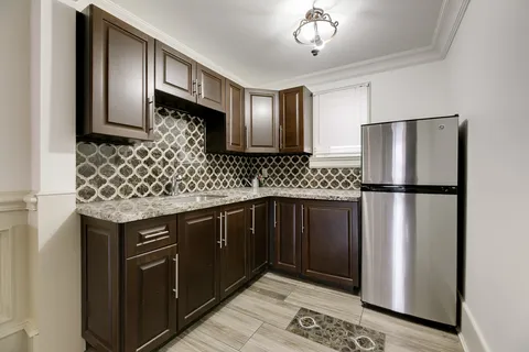 Kitchen with dark wood cabinets, patterned backsplash and a refrigerator