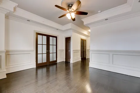Empty room with dark wood flooring, French doors and a ceiling fan