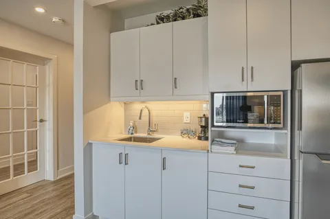 White kitchenette with cabinets, sink, refrigerator and microwave.
