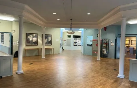Open room with wooden flooring, white columns and framed flower pictures