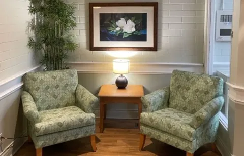 Two upholstered armchairs beside a lamp and framed flower picture