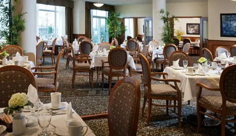 Dining room with round tables, upholstered chairs and large windows.